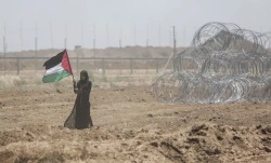 اين زن فلسطيني در اعتراض به گشايش سفارت آمريكا در فلسطين به سمت شرق غزه حركت مي‌كند و پرچمش را در دست گرفته است.